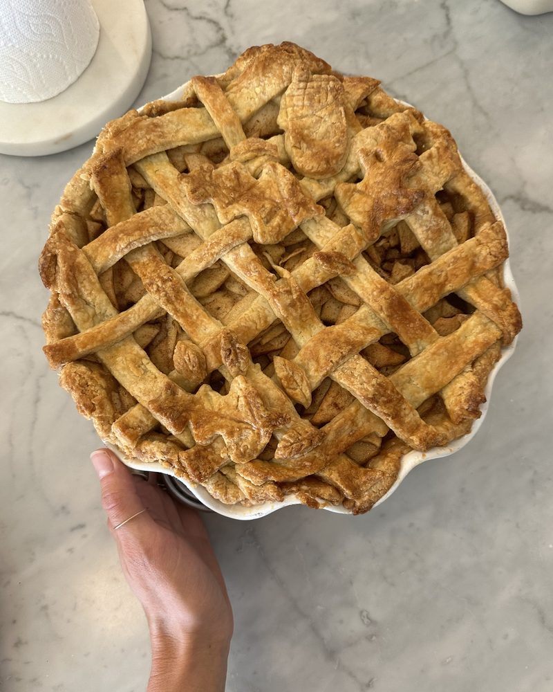 A homemade lattice-top apple pie with pastry leaves, held on a marble counter