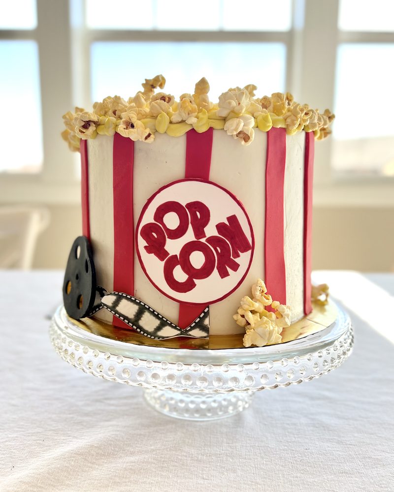 A homemade popcorn cake with red and white stripes, a film reel, and popcorn piled on top