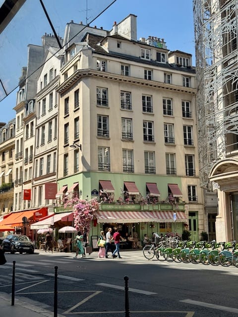A Paris corner with a café, blossom, and a rack of city bikes